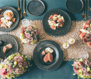 ダークグレーのクロスに料理と花を合わせた食卓の写真。提供されたレビュー画面から写真部分を切り出し、明るさのみ調整しています。